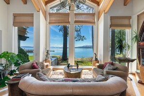 Un salon spacieux doté d’une grande fenêtre offrant une vue panoramique sur un lac et des montagnes.