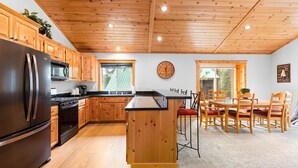 Een keuken met houten kasten, een roestvrijstalen koelkast, een houten eiland en een eethoek met houten stoelen en een tafel.