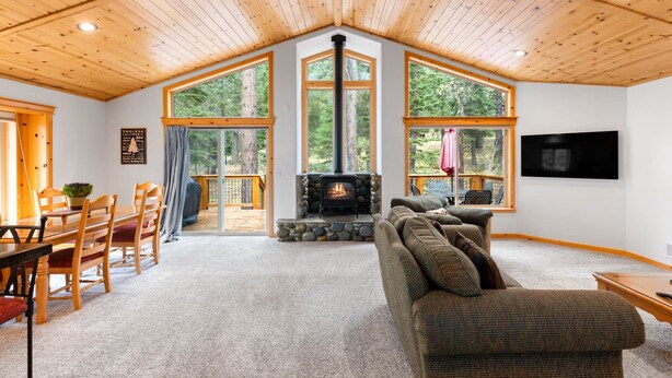 Een gezellig chaletinterieur met een stenen openhaard, houten plafond, grote ramen en een eethoek.