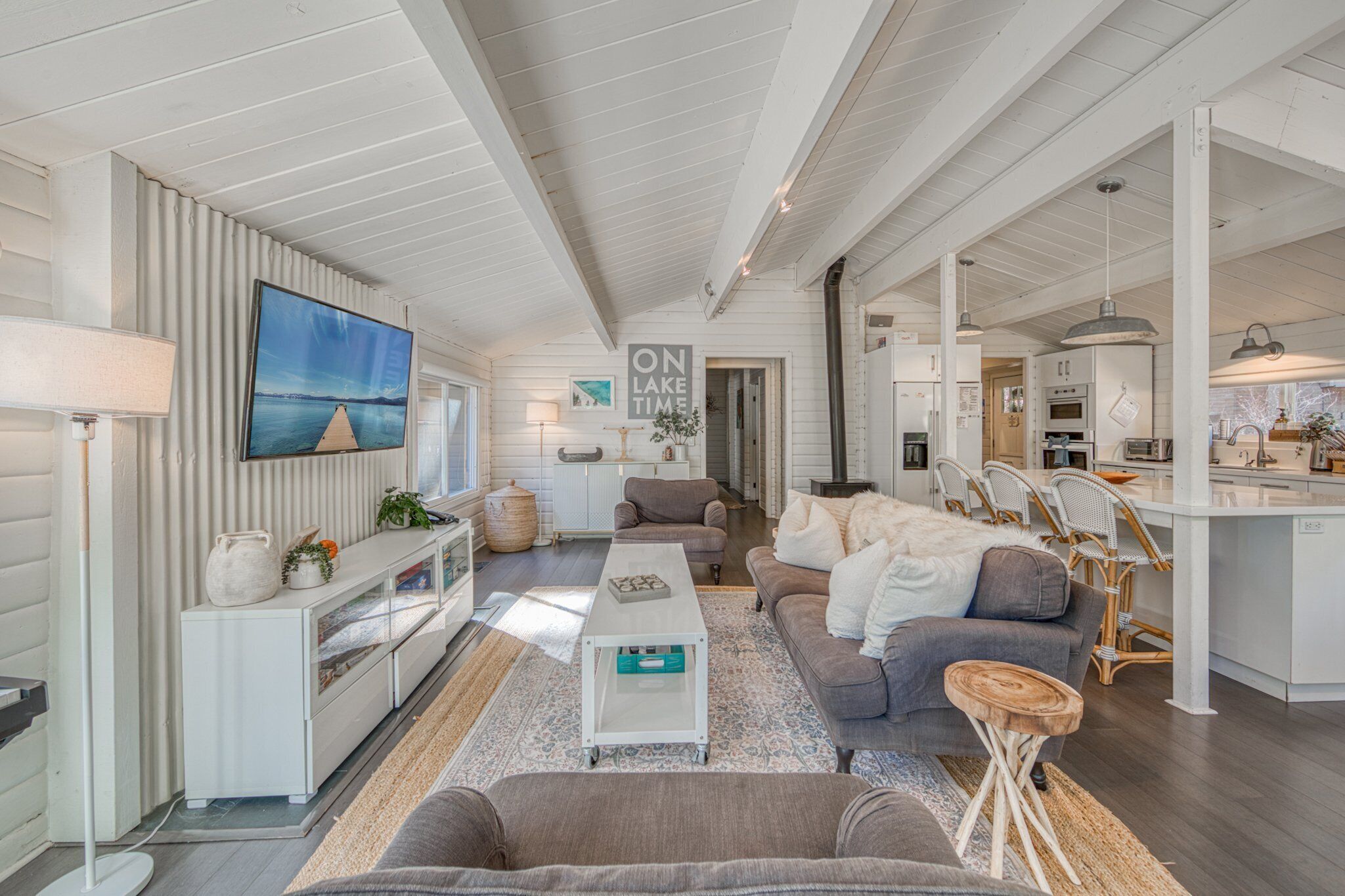 A spacious living area with a sofa, coffee table, and a TV mounted on the wall. There is a kitchen area with a dining table and chairs.