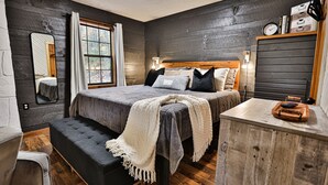 A bedroom with a large bed, a bench, a wooden dresser, a mirror, and a window with curtains. - Romantic Getaway•Views•Hot Tub•Fire Place•Seclusion (Sevierville)