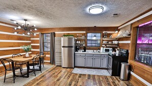 A compact kitchen with wooden walls, a dining area with a table and chairs, and a trash can. - Romantic Getaway•Views•Hot Tub•Fire Place•Seclusion (Sevierville)