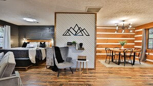 A modern hotel room with a bed, a seating area with a table and chairs, and a dining area with a wooden table and chairs. - Romantic Getaway•Views•Hot Tub•Fire Place•Seclusion (Sevierville)