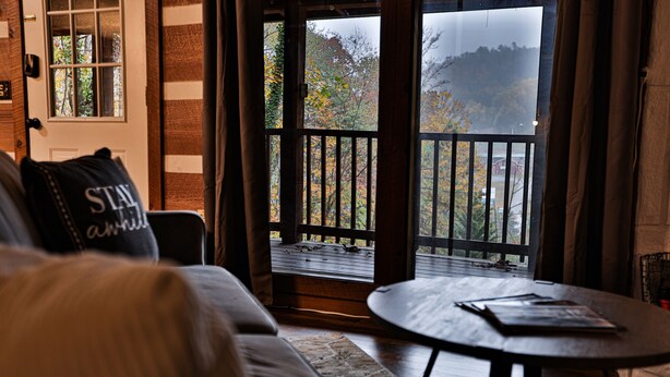 A cozy living room with a sofa, a coffee table, and a view of a balcony with a wooden railing. - Romantic Getaway•Views•Hot Tub•Fire Place•Seclusion (Sevierville)