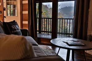 Un salon chaleureux avec un canapé, une table basse et une vue sur un balcon doté d’une balustrade en bois.