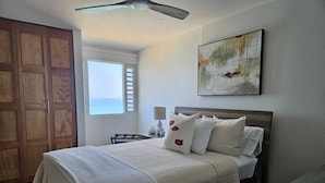 A bedroom with a bed, a ceiling fan, a window with a view, and a painting on the wall. - << NEW >> Completely Renovated, Playa Azul-Tower 1, 17th Floor, 1 Bedroom 1Bath  (Luquillo)