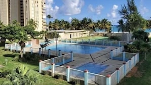 A swimming pool surrounded by a fence, with palm trees and a building in the background. - << NEW >> Completely Renovated, Playa Azul-Tower 1, 17th Floor, 1 Bedroom 1Bath  (Luquillo)