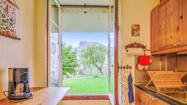 Una cocina con una mesa de madera, una cafetera y vistas a un paisaje verde con árboles y una montaña.