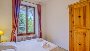 Un dormitorio con cama, ventana con cortinas, armario de madera y lámpara de noche.