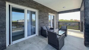 A balcony with a modern design, featuring a glass door, wicker furniture, and a view of the cityscape.