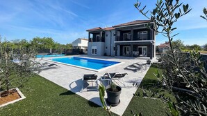 A two-story house with a swimming pool, outdoor seating, and a well-maintained garden.