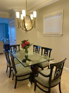 Una sala da pranzo con un tavolo in vetro circondato da sedie, un lampadario e una finestra con persiane.