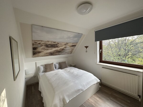 A bedroom with a bed, a window with a view of trees, a radiator, and a painting on the wall.