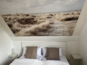 A bedroom with a bed, two pillows, a nightstand, and a wall-mounted shelf.