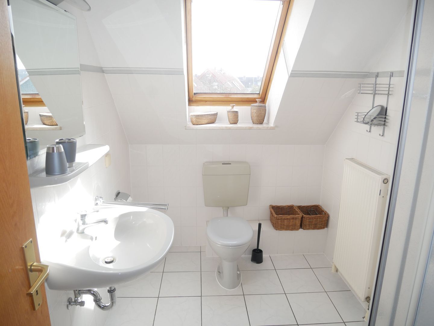 Une salle de bain moderne avec un puits de lumière, des carreaux blancs, un lavabo, des toilettes et des paniers de rangement.