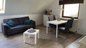 Una sala de estar moderna con un sofá gris, una mesita blanca y un comedor con una mesa y sillas blancas.