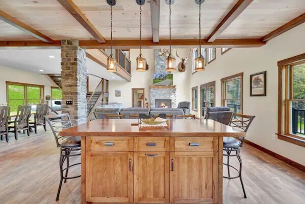 A spacious living area with a large wooden island, stone fireplace, and multiple windows.