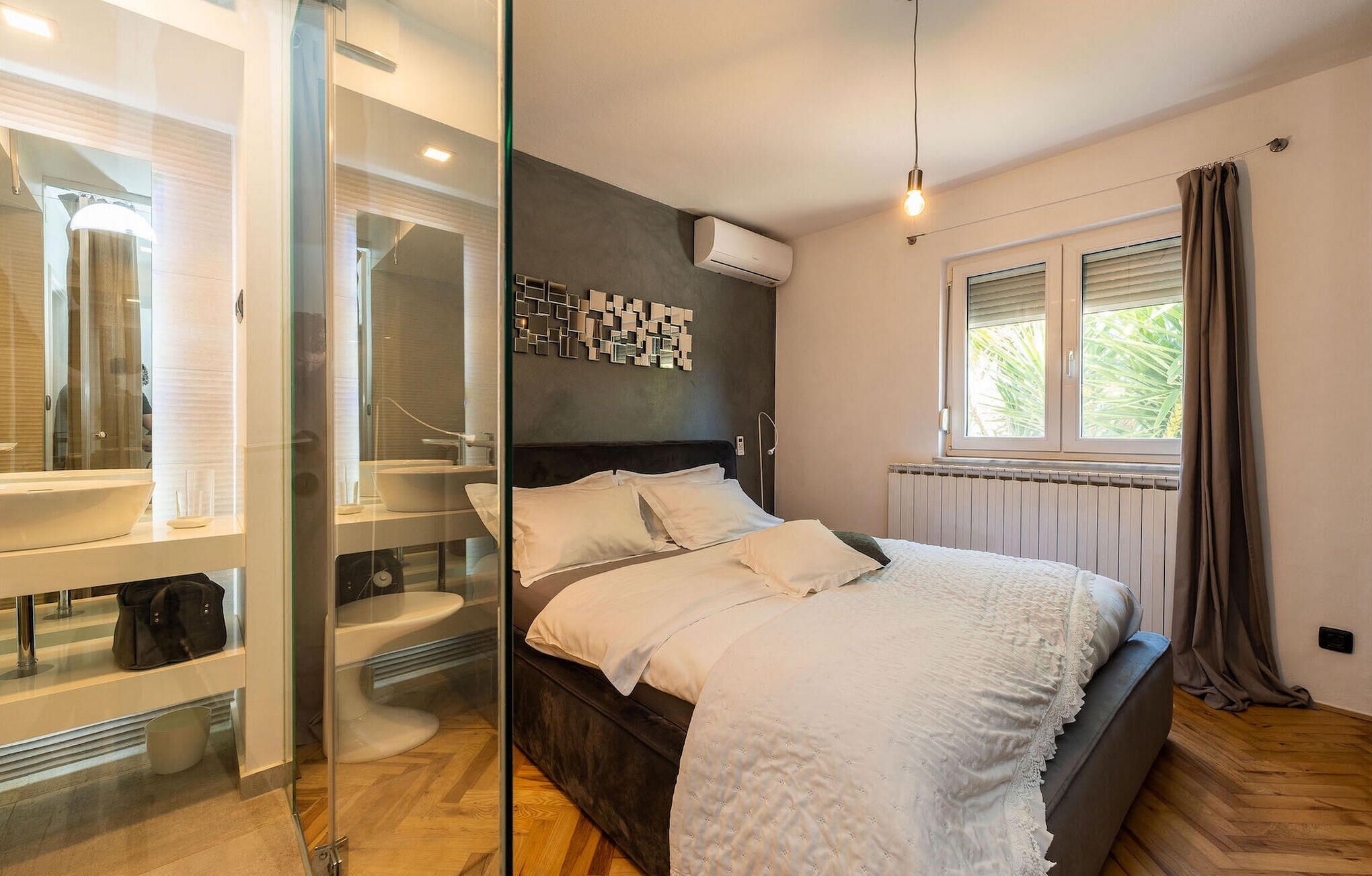 Een moderne slaapkamer met een groot bed, een badkamer met glazen wanden en een raam met gordijnen.