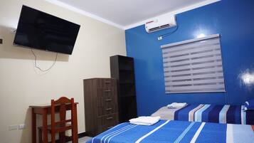 Una habitación con cama, escritorio, silla, televisor y aire acondicionado.