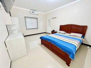 Un dormitorio con cama de madera, mesita de noche, armario y una ventana con persianas, además de un equipo de aire acondicionado.