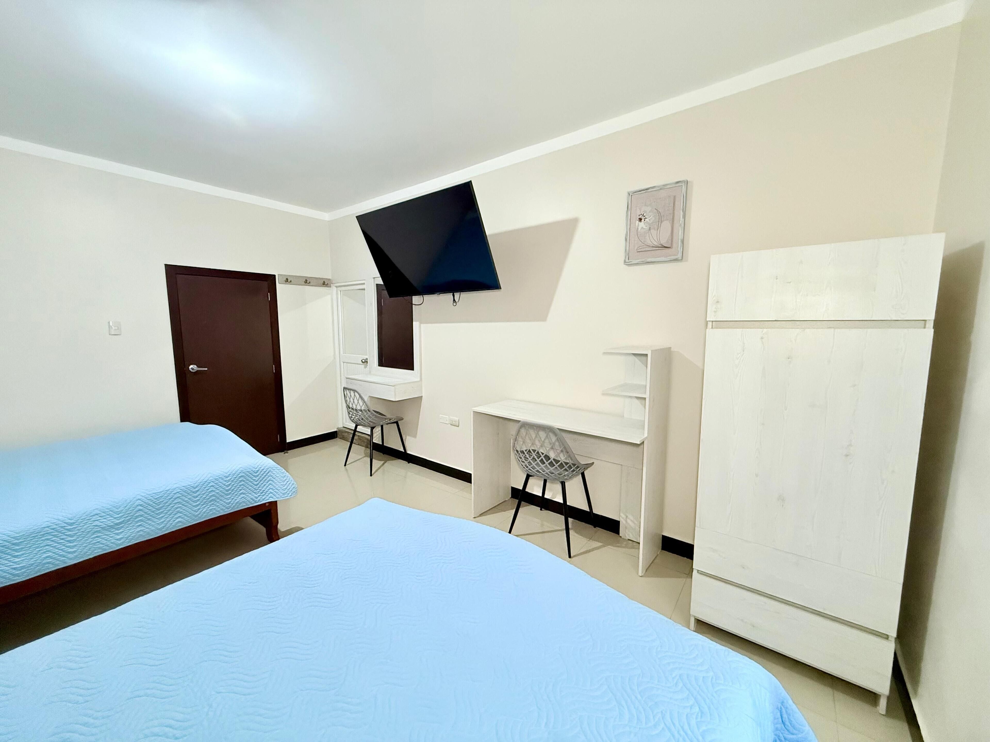 A bedroom with two beds, a desk, a chair, a TV, and a wardrobe.