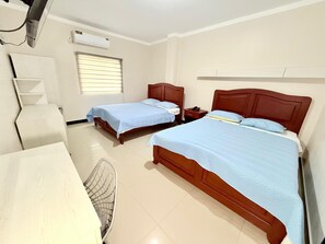 Habitación de hotel con dos camas de madera, un escritorio, una silla, un equipo de aire acondicionado y una ventana con persianas.
