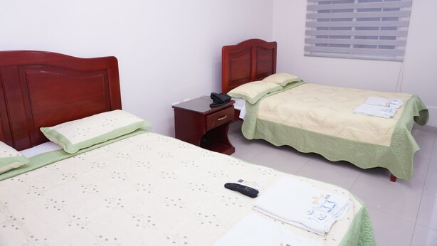 Une chambre avec deux lits simples, une table de chevet, une commode et une fenêtre avec des stores.