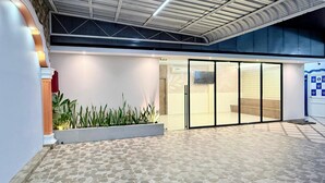 Una entrada moderna de edificio con suelo de baldosas de piedra, puerta de cristal y una jardinera con plantas.