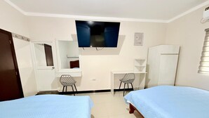 Un dormitorio con dos camas, un escritorio, una silla, un televisor, un armario y una ventana.