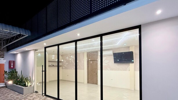 Un edificio moderno con amplias puertas de vidrio, una zona de recepción con televisor de pantalla plana y un patio con suelo de piedra.