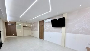 Una habitación moderna y espaciosa con televisor de pantalla plana en la pared, un mostrador de recepción de madera y un letrero que dice "SMIR".