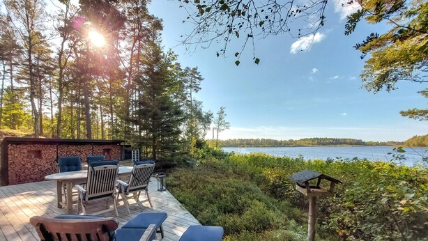 A deck with outdoor seating, a stone wall, and a view of a lake. - Stunning home in Skånes Fagerhult (Skånes Fagerhult)