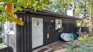 A small wooden cabin with a white door, a broom hanging on the door, and a surfboard leaning against the wall. - Stunning home in Skånes Fagerhult (Skånes Fagerhult)