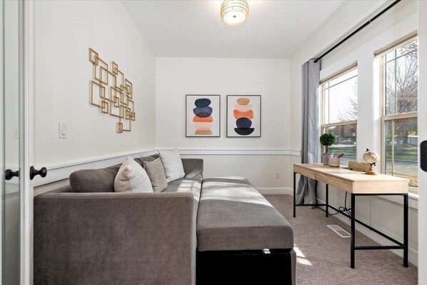 A modern living room with a gray sectional sofa, a wooden desk, and abstract wall art.