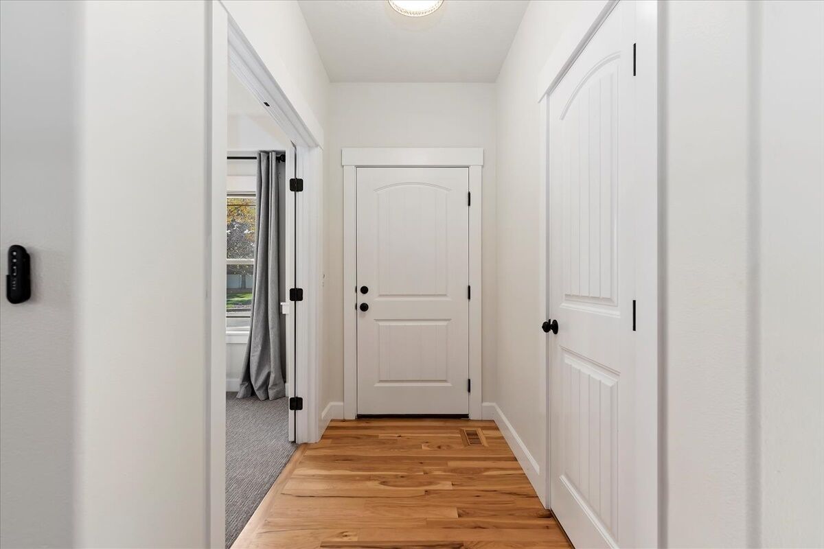 A narrow hallway with a wooden floor, white walls, and a white door with black handles.
