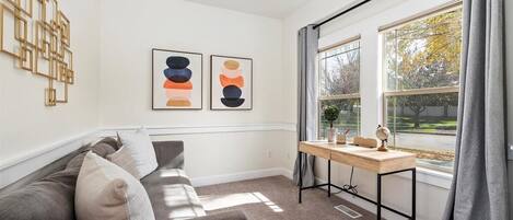 A modern living room with a grey sofa, two abstract paintings, a wooden side table with a globe, and a window with curtains.