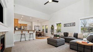 Ein geräumiges Wohnzimmer mit Kamin, einem grauen Sofa, einem Couchtisch und einer Küche im Hintergrund.