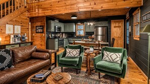 L’intérieur chaleureux d’un chalet comprend un salon avec un canapé en cuir et des fauteuils verts, une table à manger en bois et une cuisine équipée d’appareils électroménagers modernes.