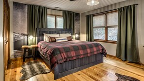 Ein Schlafzimmer mit einem hölzernen Bett, grünen Vorhängen und einem Fellteppich.