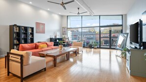Ein geräumiges Wohnzimmer mit großem Fenster, Deckenventilatoren, einer Couch, einem Couchtisch und einem Bücherregal.