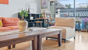 Ein modernes Wohnzimmer mit Sofa, Sessel, Couchtisch und einem großen Fenster mit Blick ins Freie.