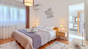 A bedroom with a bed, bedside lamps, a wall-mounted air conditioner, and a view of a balcony through a glass door. - Amazing home in Krsan (Krsan)