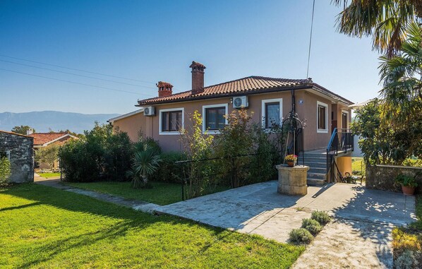A two-story house with a tiled roof, a chimney, and a small garden with a pathway leading to the entrance. - Amazing home in Krsan (Krsan)
