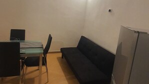 Un ambiente compatto con un tavolo da pranzo e sedie, un divano scuro e un frigorifero.