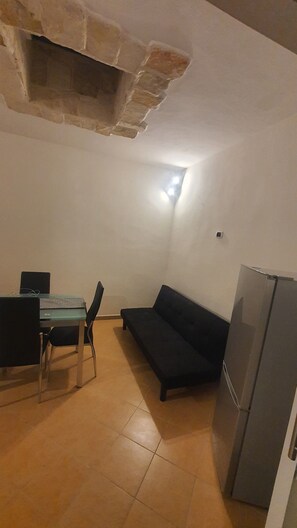 Ett kompakt vardagsrum med ett matbord och stolar, en mörk soffa och ett kylskåp.