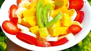 Una mano che tiene una ciotola di insalata di frutta con fragole, banane, manghi e kiwi.