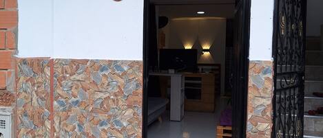 Entrada de um prédio com chão de tijolos de pedra, uma placa indicando o apartamento número 19 e um portão preto que dá acesso ao interior.