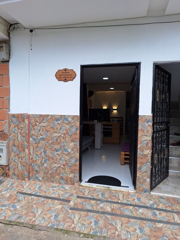A building entrance with a stone-tiled ground, a sign indicating apartment number 19, and a black gate leading inside.