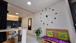 Una stanza moderna con una panca di legno, una sveglia a muro e un tavolino con un bicchiere.