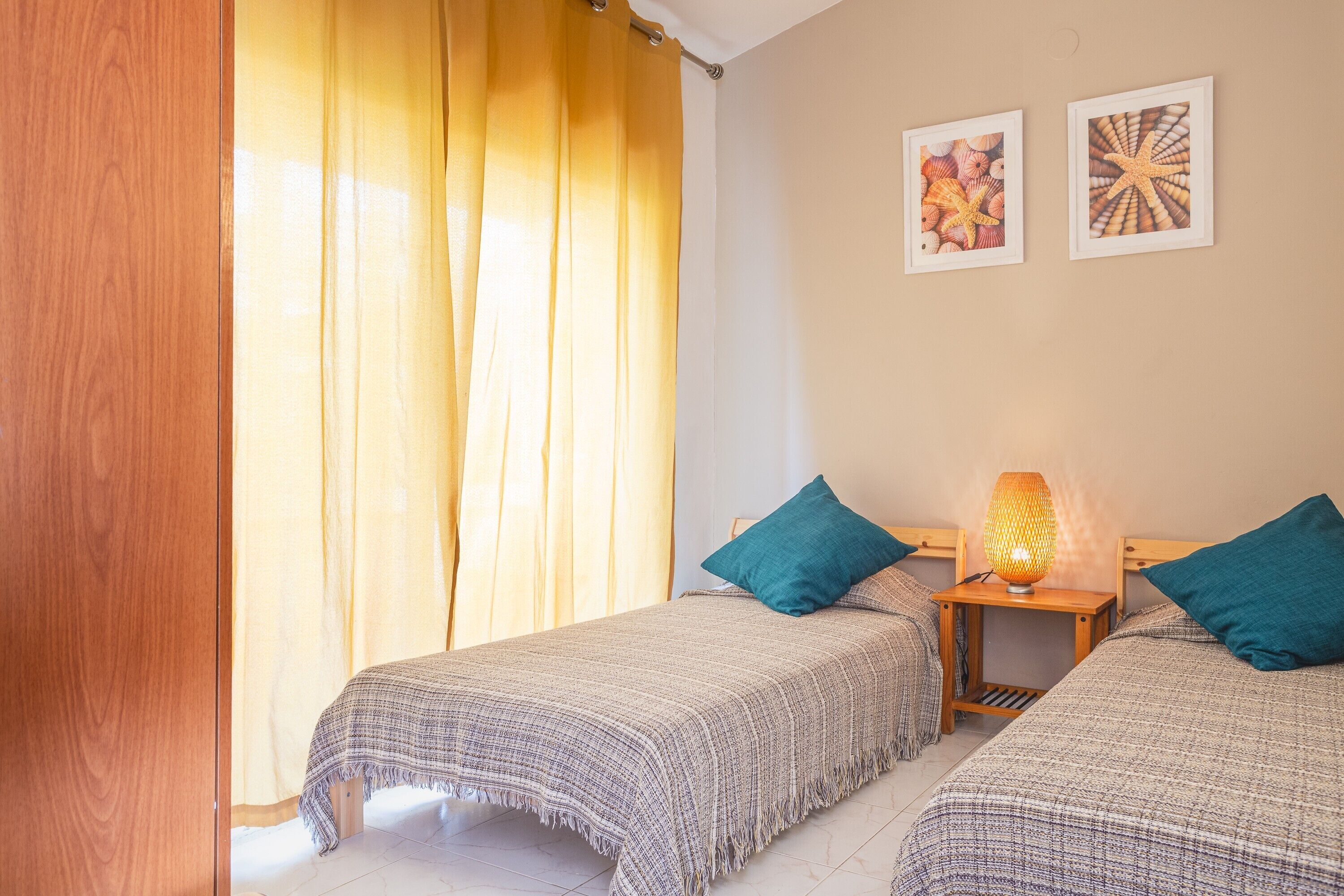 A bedroom with two beds, a nightstand with a lamp, and two framed pictures on the wall.
